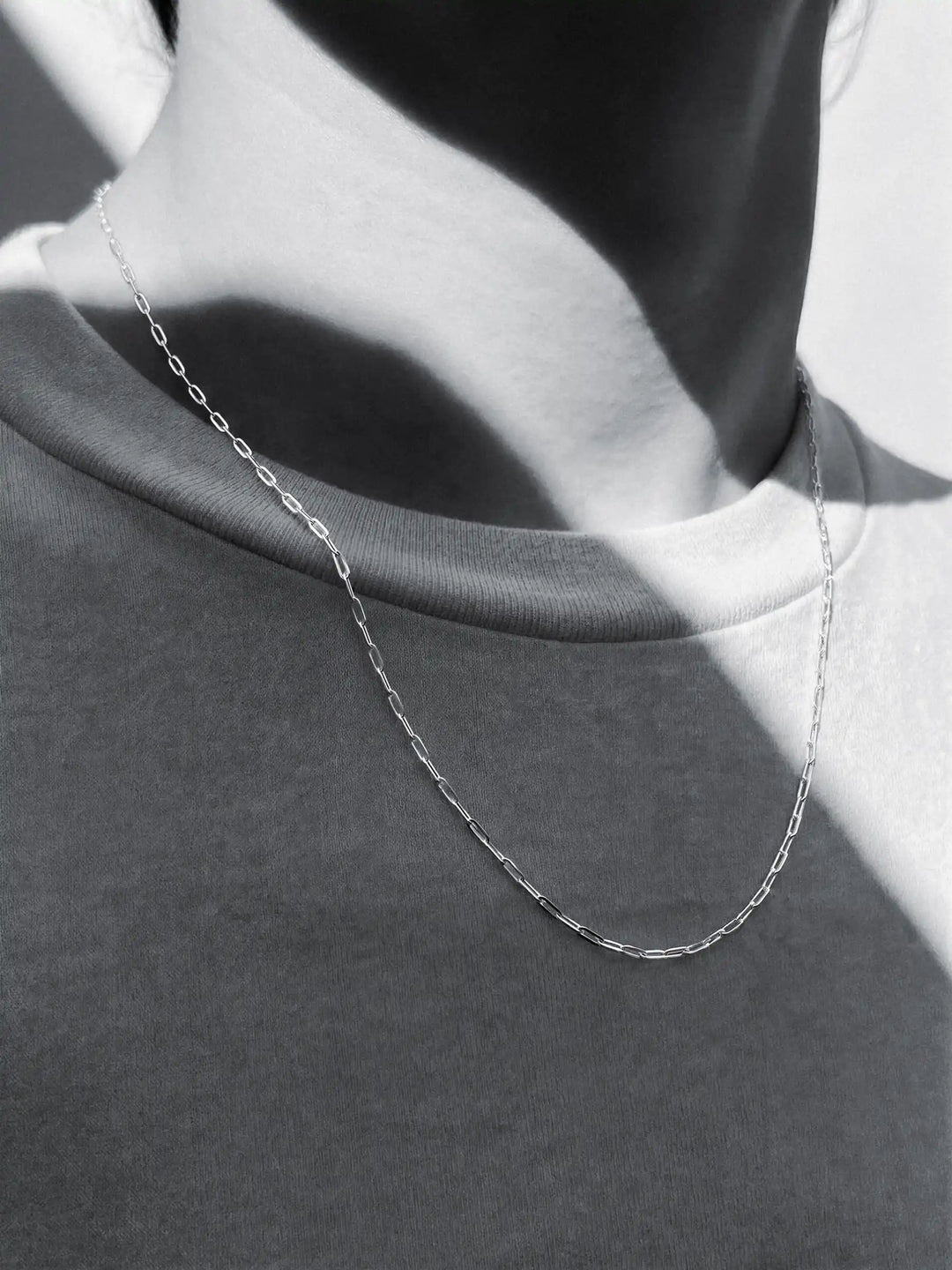 Silver chain necklace on a person with a plain background