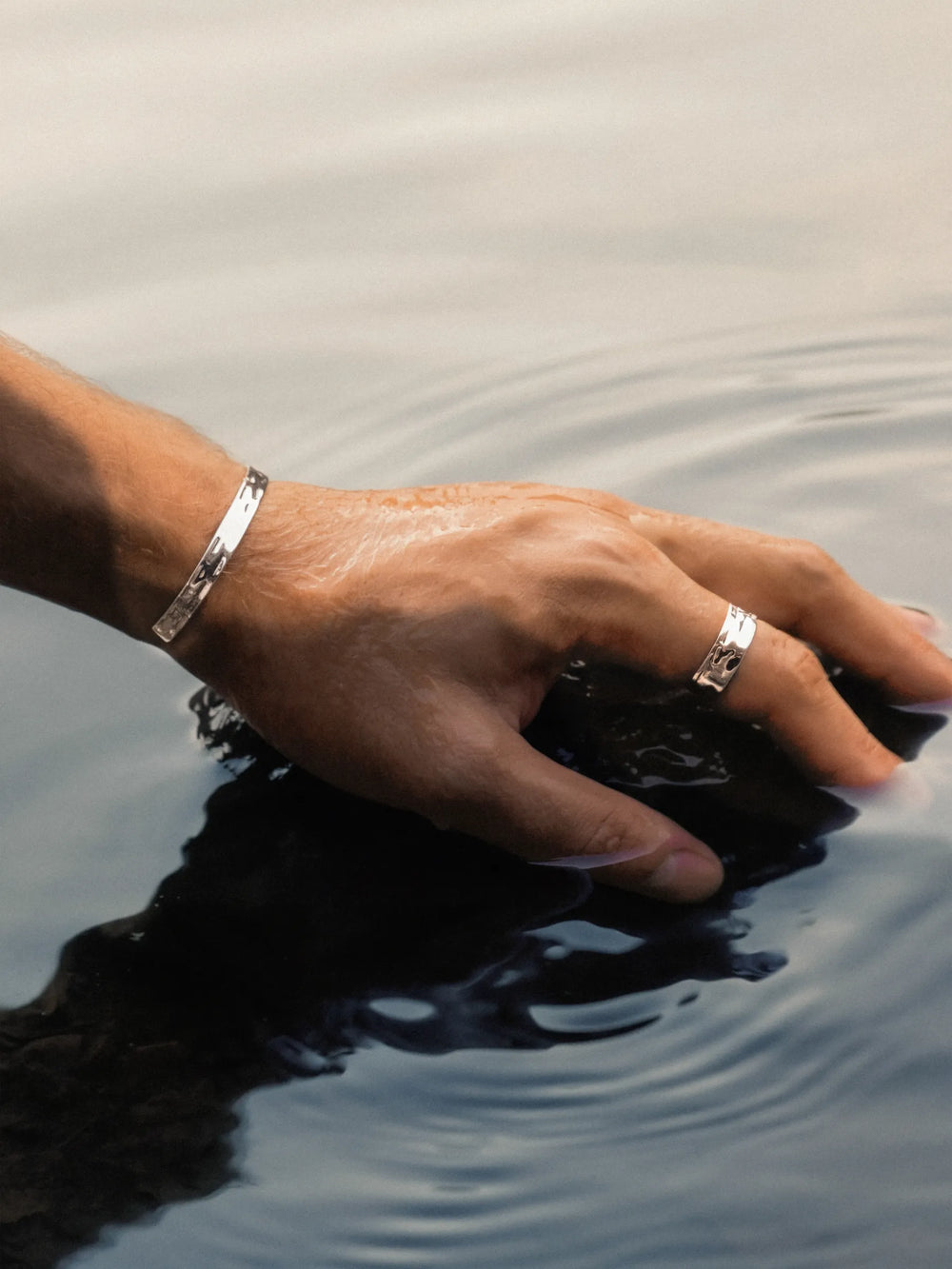 Hand with silver ring and bracelet touching water