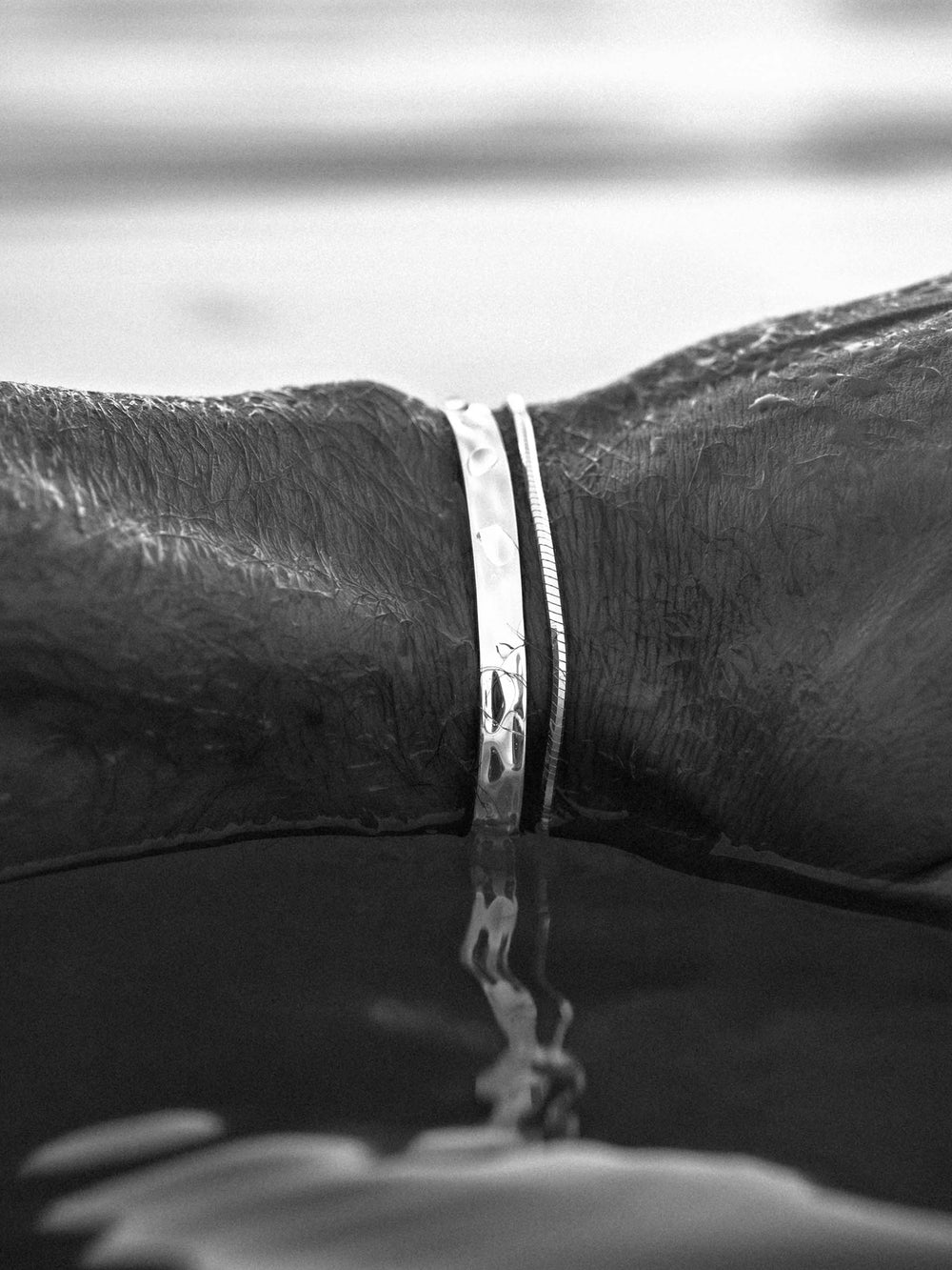 Close-up of a hand wearing silver cuff and bracelet touching water surface