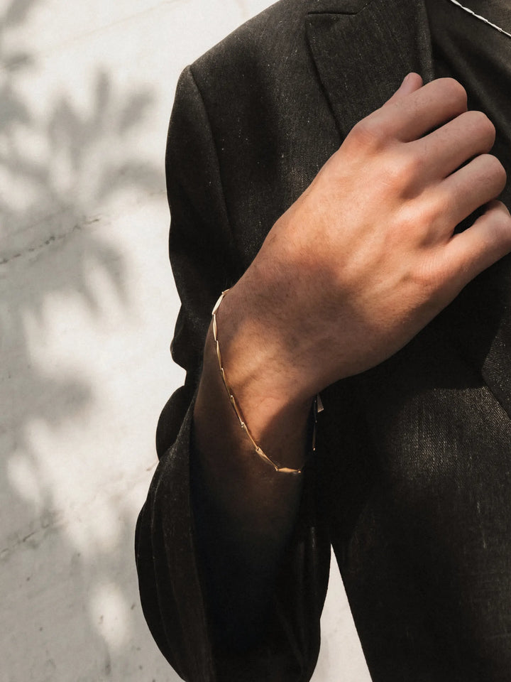 Hand wearing a gold bracelet against a dark coat