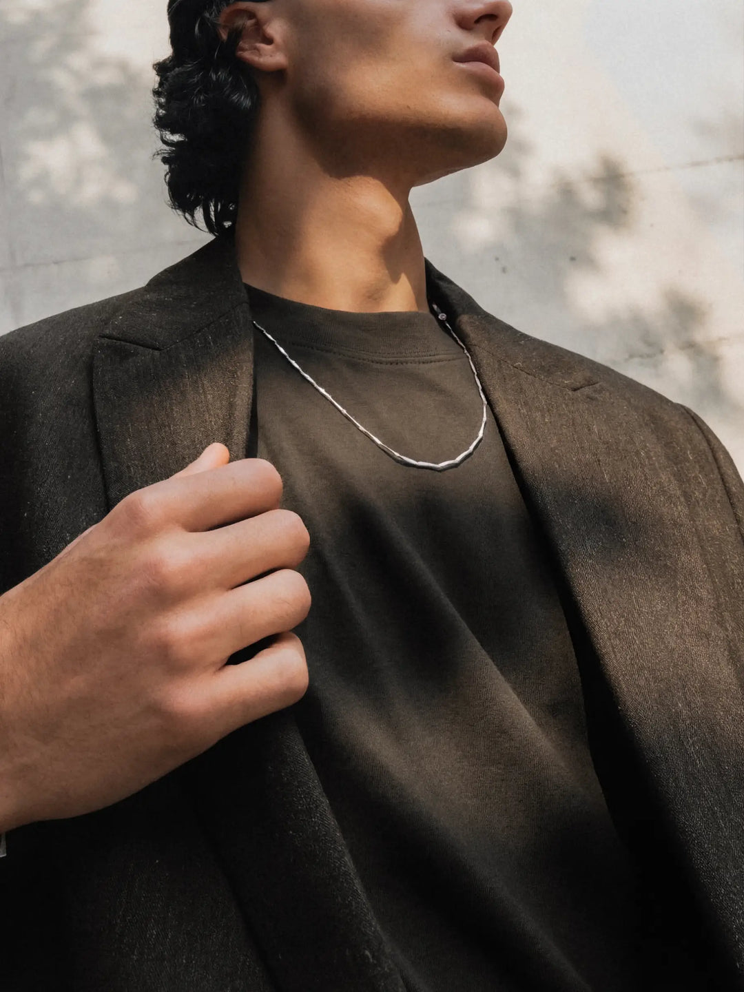 Person wearing a silver necklace with a dark shirt and coat