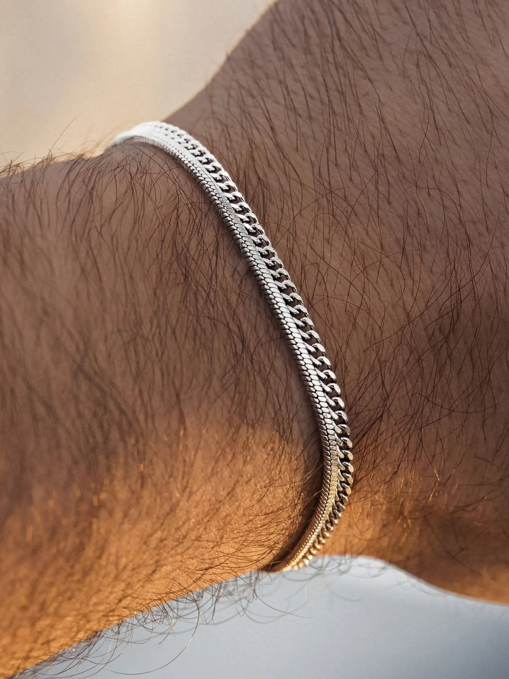 Two silver chain bracelets on a person's wrist against a blurred background