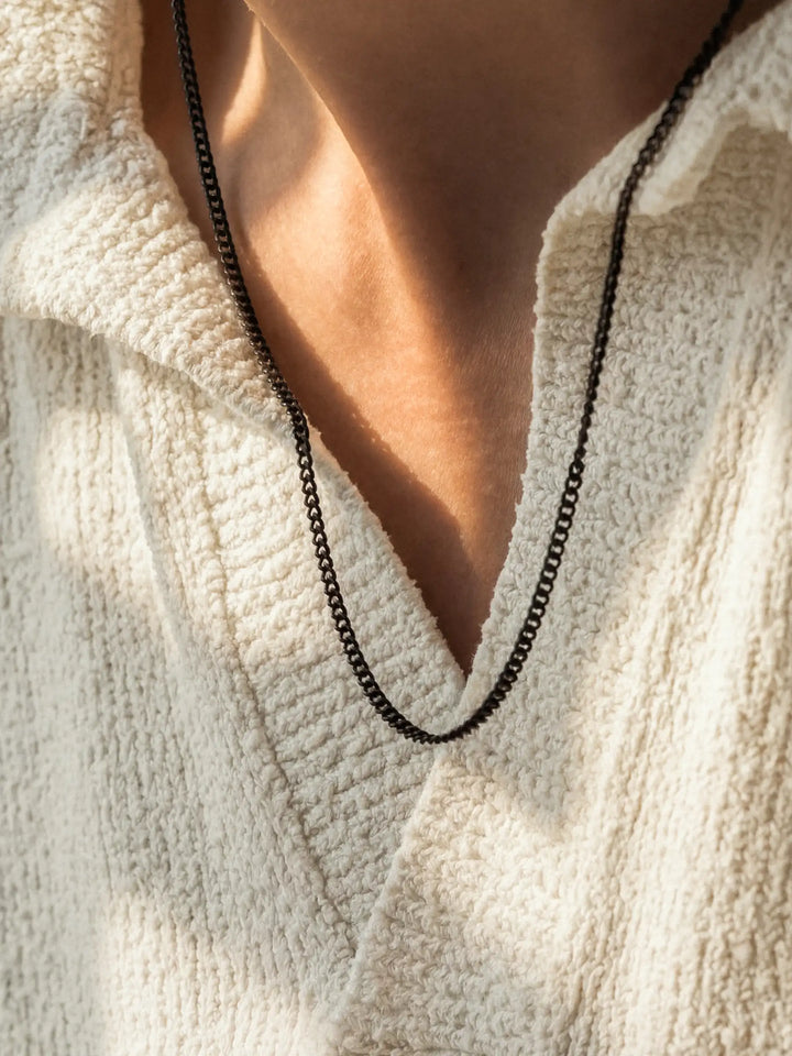 Close-up of a person wearing a black chain necklace with a light-colored garment.