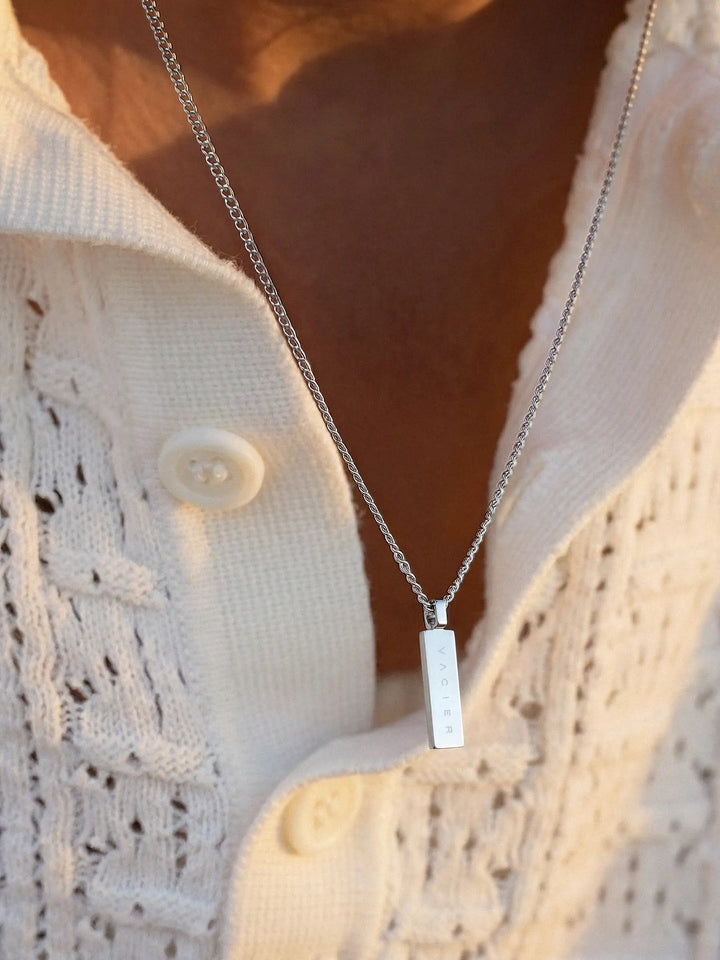 Silver necklace with a rectangular pendant on a person wearing a white cardigan.