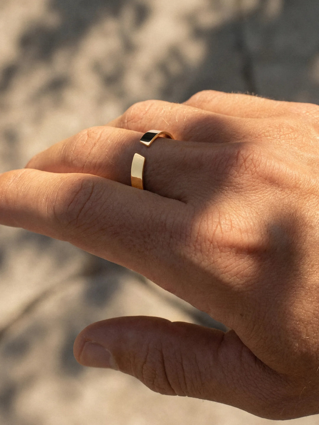 Hand wearing a gold ring with a blurred natural background