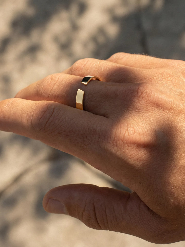 Hand wearing a gold ring with a blurred natural background