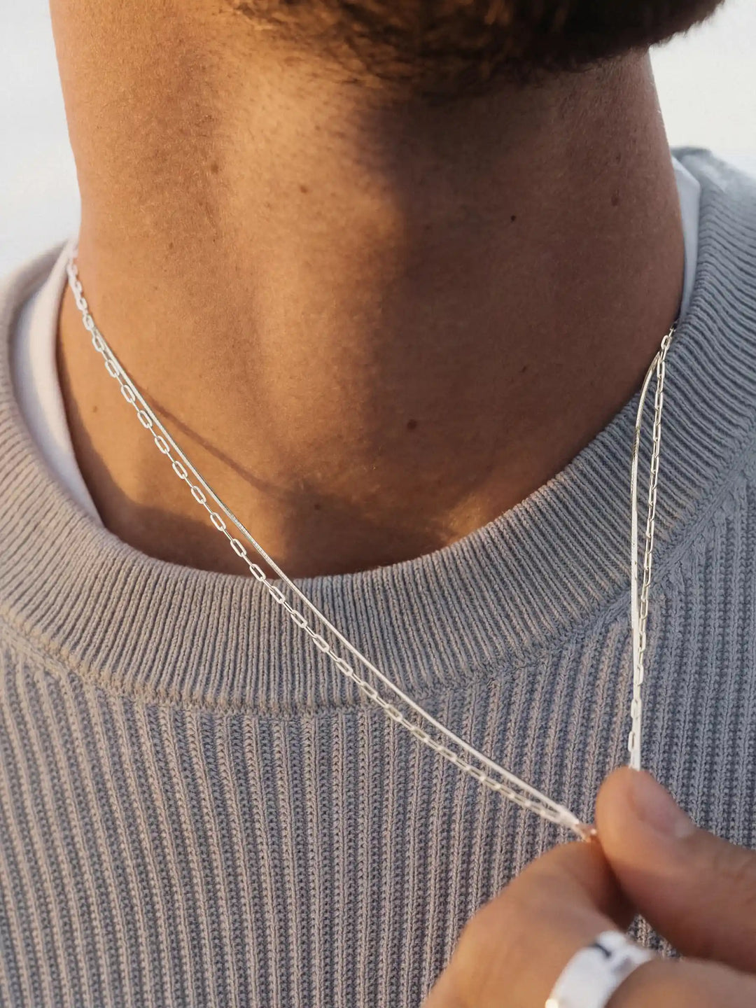 Close-up of a person's neck wearing two silver necklaces