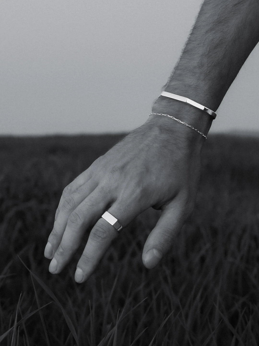 Hand wearing a silver ring, cuff and bracelet with a natural background