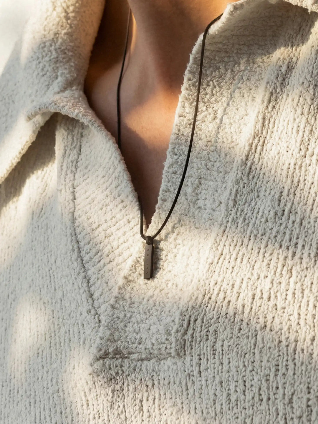 Person wearing a black necklace with a rectangular pendant and a light-colored sweater