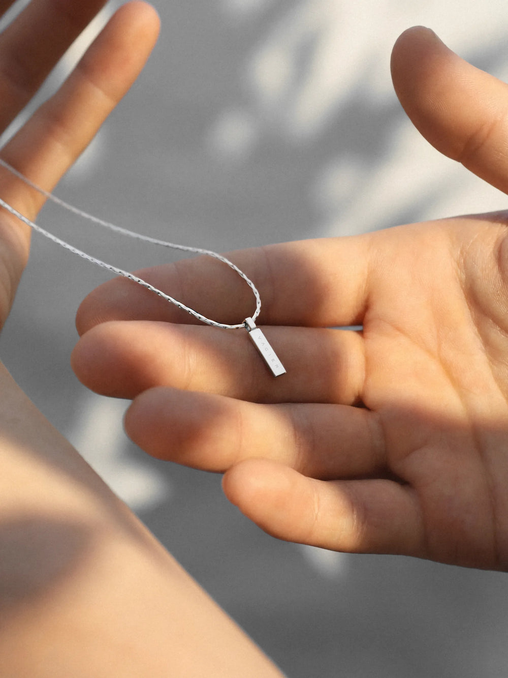 Hand holding a silver necklace with a rectangular pendant