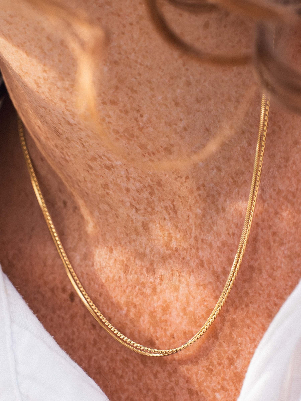 A gold and a silver chain necklace on a person's neck 