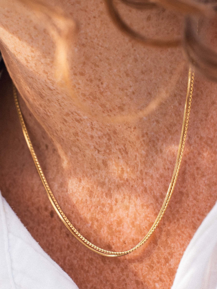 A gold and a silver chain necklace on a person's neck 