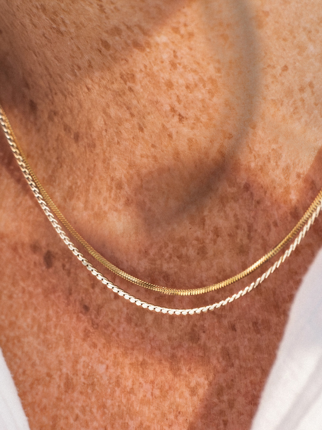 A gold and a silver chain necklace on a person's neck