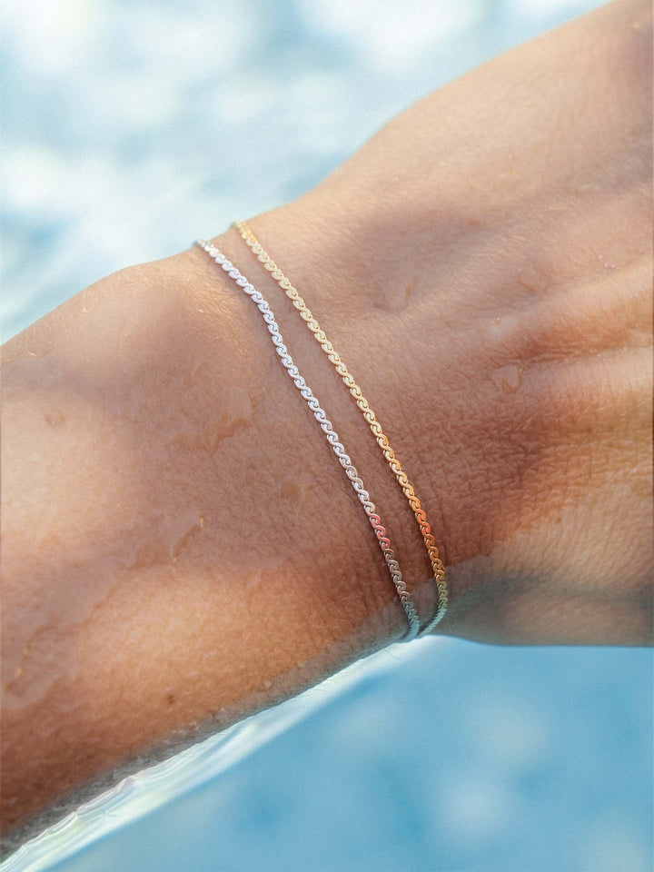 Close-up of a person's arm with two thin bracelets against a blurred pool background