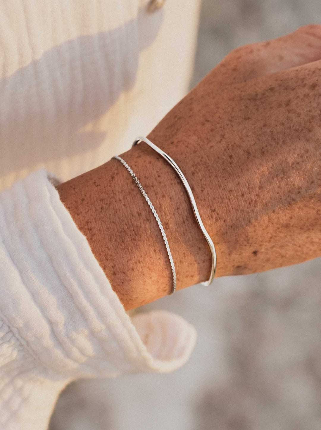 Silver cuff and bracelet against a light-colored garment