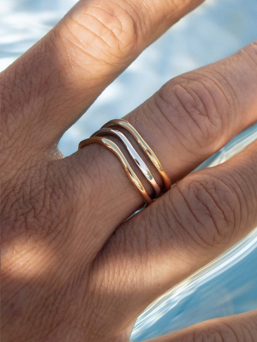 Close-up of a hand wearing two gold and a silver ring with a blurred natural background