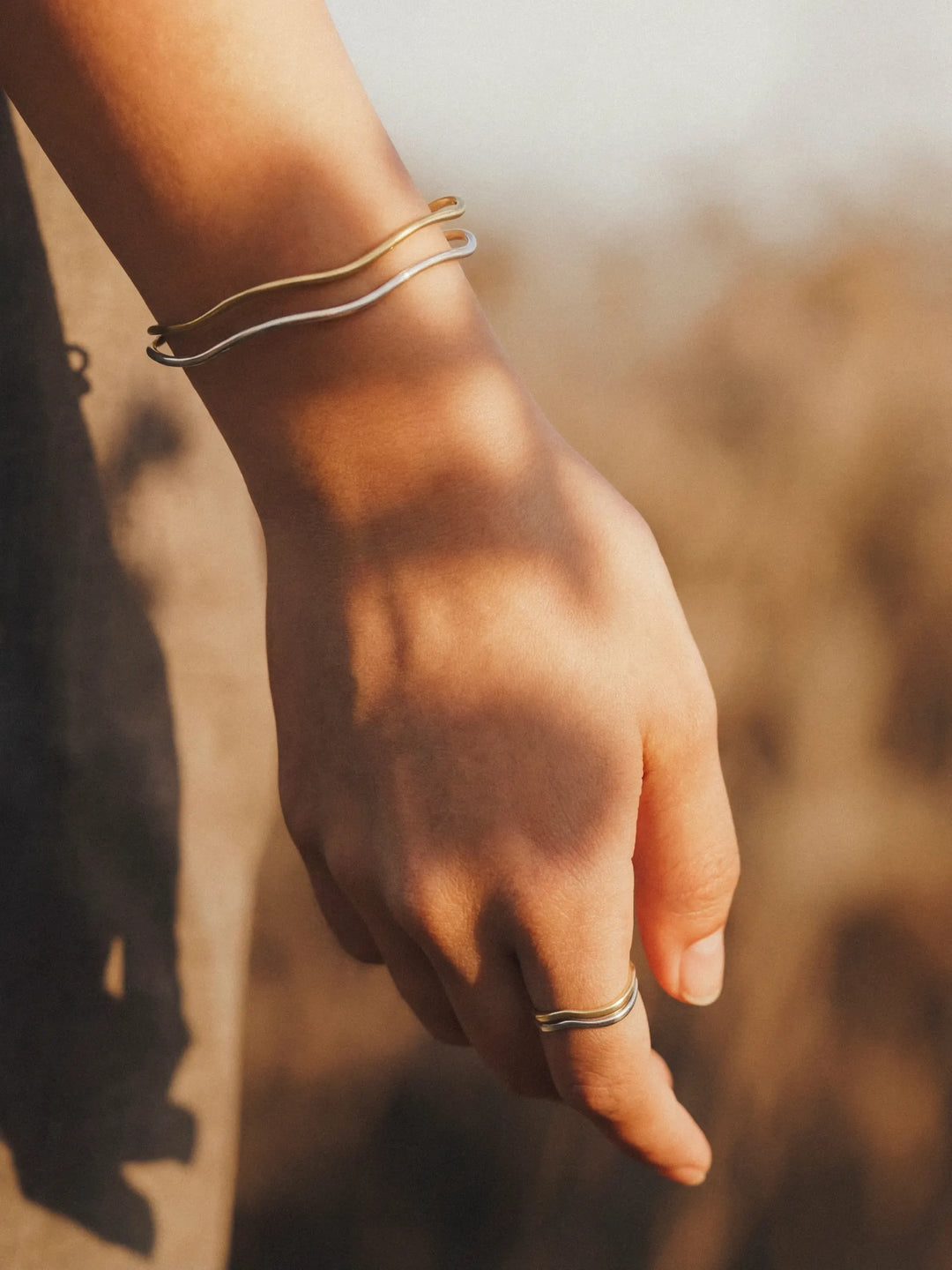 Hand with gold and silver cuffs and rings against a blurred natural background