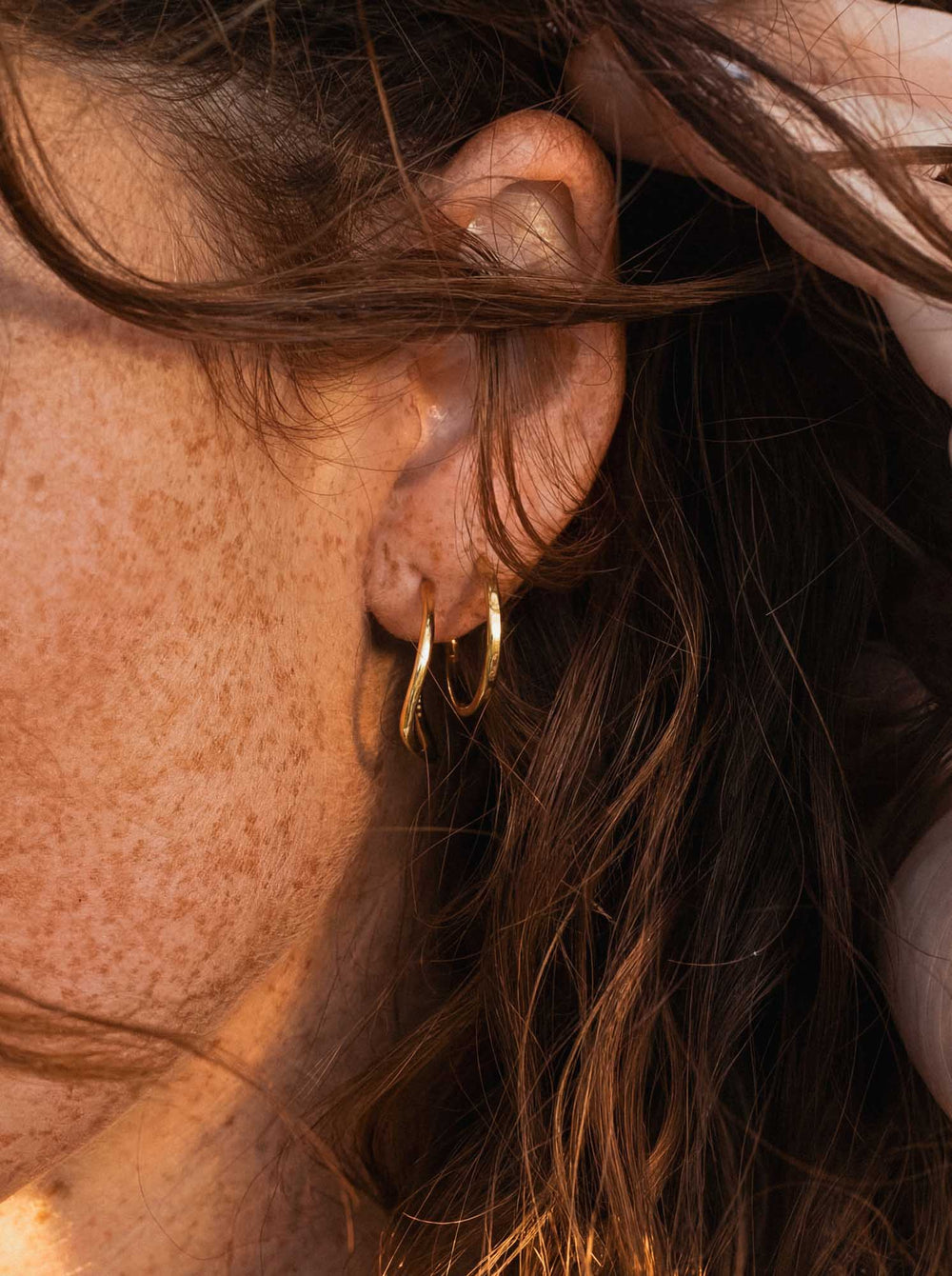 Close-up of a person wearing gold hoop earrings with sunlight casting shadows.