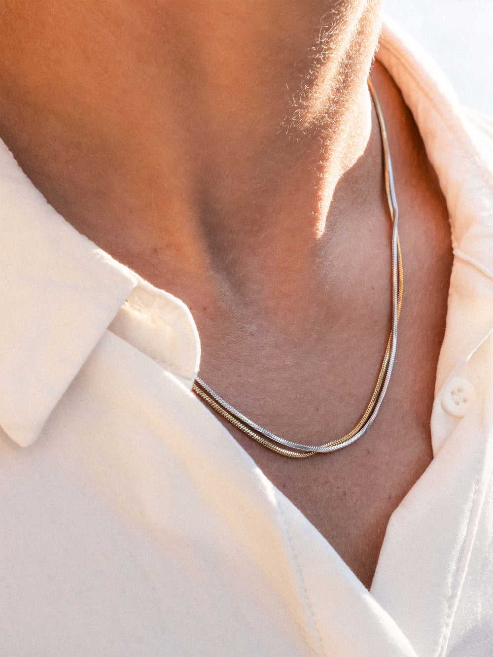 Close-up of a person wearing a silver  and a gold necklace with a light-colored shirt.